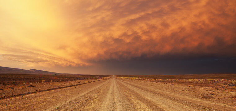 A wide angle view of a huge thunder storm building over a lone dirt road in the Greater Karoo of South Africa