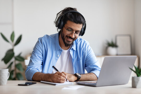 Western Guy Wearing Headphones Studying Online With Laptop At Home, Taking Notes