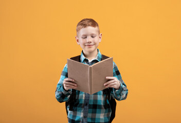 Obraz premium Joyful schoolboy reading book, yellow studio background