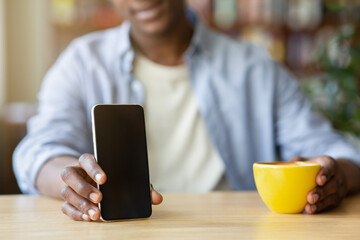 Cropped view of young black guy holding smartphone with blank screen at cafe, mockup for mobile app design