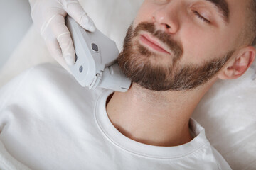 Cropped close up of a bearded man smiling while cosmetologist using skincare laser apparatus on his face