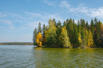 Autumn forest trees are reflected in the river water of the panoramic landscape. Blue sky with clouds.