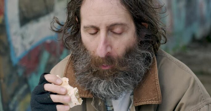 Man with a beard sitting outside eating food relived to be satisfying his hunger