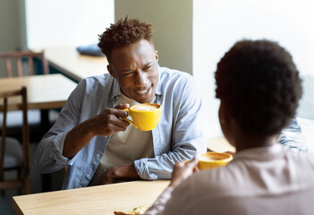 Fototapeta na wymiar Attractive black guy with his girlfriend drinking coffee and having pleasant conversation at urban cafe