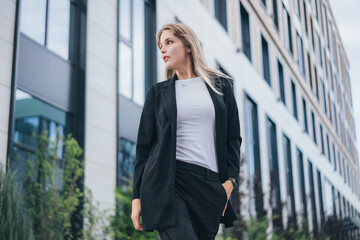 a cute blonde in a business black suit walks around the territory of a business center
