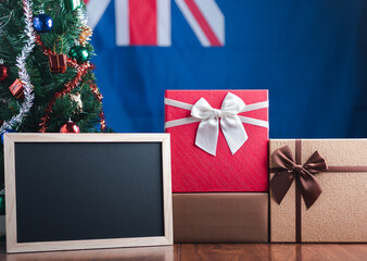 Small blackboard and gift boxes on wooden table with a Christmas tree and Australian flag in the background. Space for text. Concept of Christmas and new year festival
