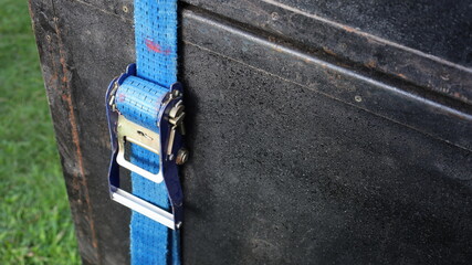Blue ratchet strap. Closeup ratchet tie down secures stacked black speaker cabinets with copy space.
