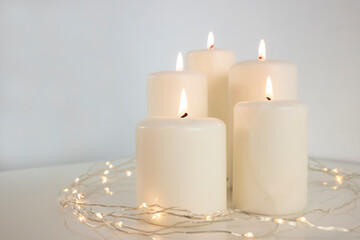 Large burning candles and Christmas garland on a white background. Side view, space for text.