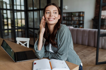 Beautiful smiling woman talking on cellphone while working with laptop