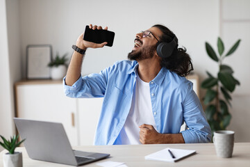 Cheerful Indian Guy Listening Music And Singing While Working At Home Office