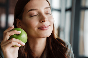 Beautiful happy nice woman smiling at camera while eating apple