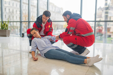 Male medical workers in red uniform making an injection to a faint woman