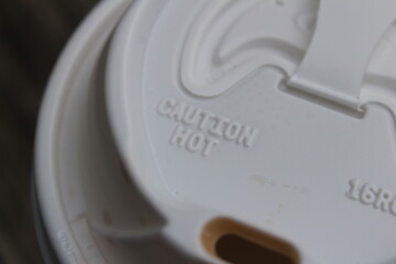 A plastic to go coffee lid with a warning label that reads 'caution hot'.