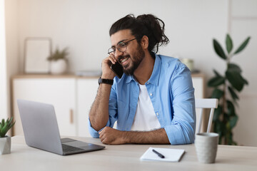 Western Freelancer Guy Talking On Cellphone And Working On Laptop At Home