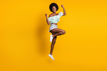 Fototapeta na wymiar Full length body size photo of jumping cheerful crazy girl gesturing like winner isolated on bright yellow color background