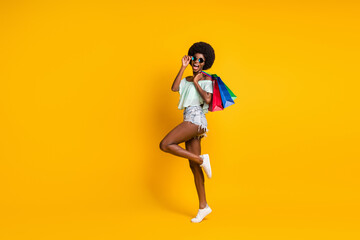 Fototapeta na wymiar Full length body size photo of black skinned girl holding packages sale black friday isolated on vibrant yellow color background copyspace