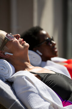 Senior woman with earbud headphones sunbathing on sunny patio
