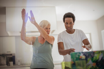 Senior women friends exercising online at laptop in kitchen