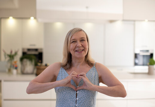Portrait beautiful happy senior woman gesturing heart shape in kitchen