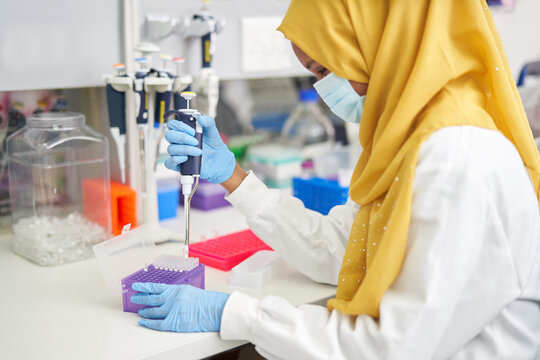 Female scientist in hijab and face mask using pipette in laboratory