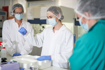 Female scientists in face masks and protective workwear in laboratory
