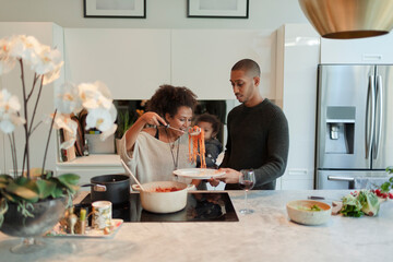 Couple with baby daughter cooking spaghetti in kitchen