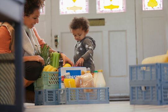 Curious baby daughter watching mother unpack crate of groceries