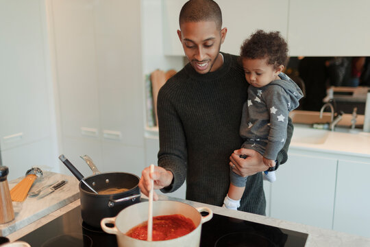 Happy father holding baby daughter and cooking spaghetti at stove