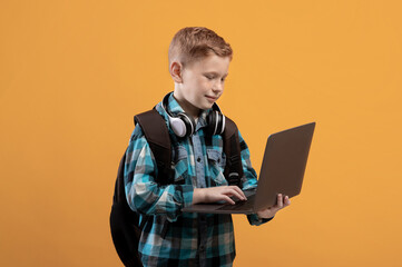 Smart schoolboy with backpack and headset holding laptop