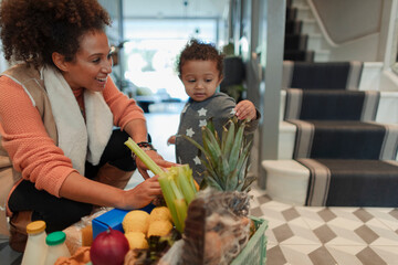 Cute baby daughter helping mother unpack grocery delivery