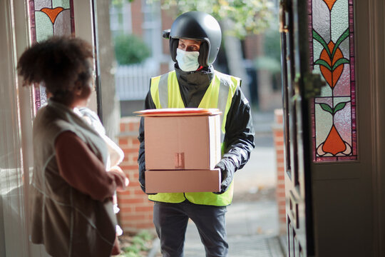 Woman receiving packages from delivery man in face mask at front door