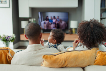 Parents and baby daughter watching TV on living room sofa