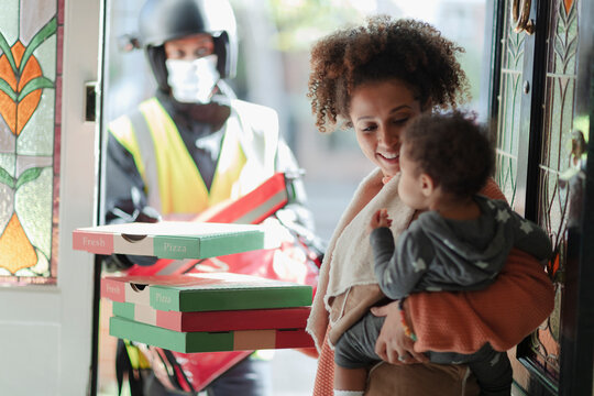 Mother and baby daughter receiving pizza delivery at front door