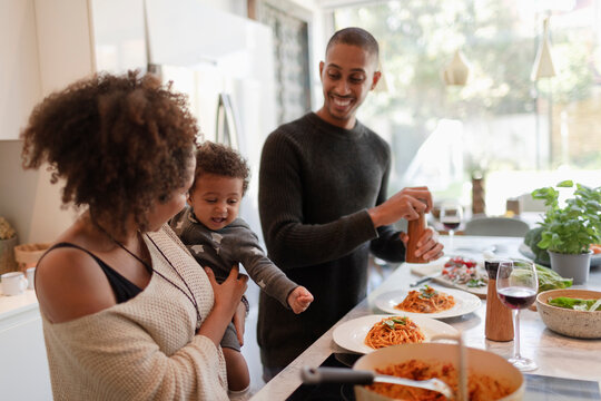 Happy parents with baby daughter cooking spaghetti in kitchen