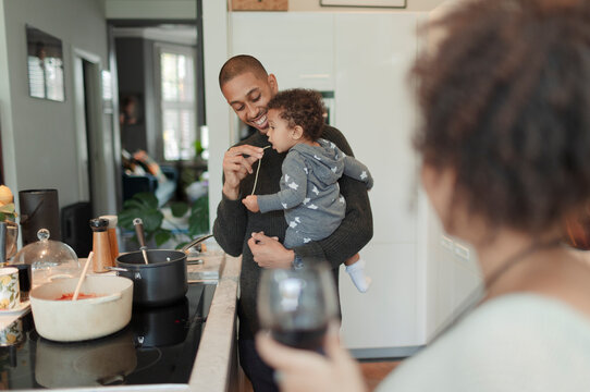 Father cooking and feeding baby daughter at kitchen stove