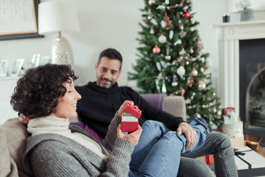 Wife opening Christmas gift from husband on living room sofa