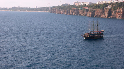 Obraz premium Beautiful yacht with tourists floating on the sea. Blue wavy sea with resort town in the background. Summer vacation concept. Travel to Turkey.
