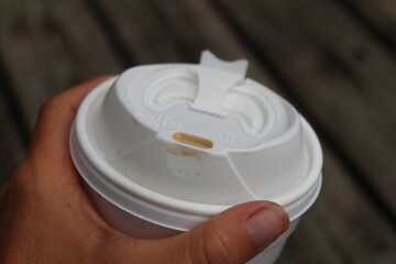 A female hand holding a plastic to go cup of coffee against a dark rustic wooden background.