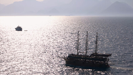 Boat with tourists floating on the sea. Sea water ripples with sun reflections. Fog and mountains in the background. Antalya, Turkey.