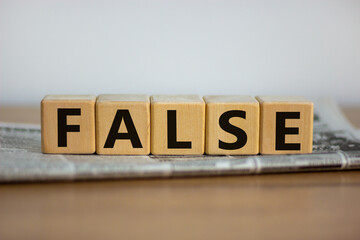 False in news symbol. Cubes placed on a newspaper form the word 'false'. Beautiful wooden table. White background. Business and false in news concept. Copy space.