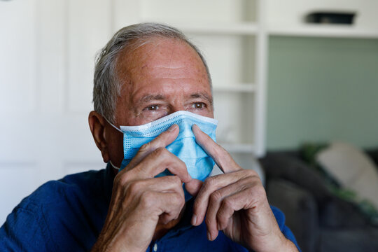 Senior Caucasian Man Wearing Face Mask Touching His Nose At Home