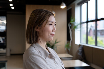 Asian woman looking out of window in creative office cafeteria