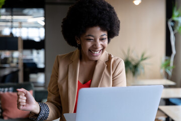 Cheering mixed race businesswoman using laptop during video call in office