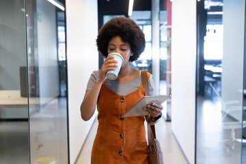 Mixed race businesswoman using tablet drinking coffee in creative office