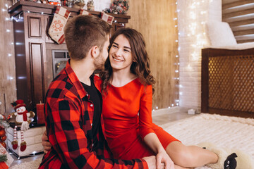 Christmas. A young couple greeting each other with a tender kiss, they exchange Christmas presents. The brick wall in the room is decorated with Christmas lights. Merry Christmas and Happy New Year.