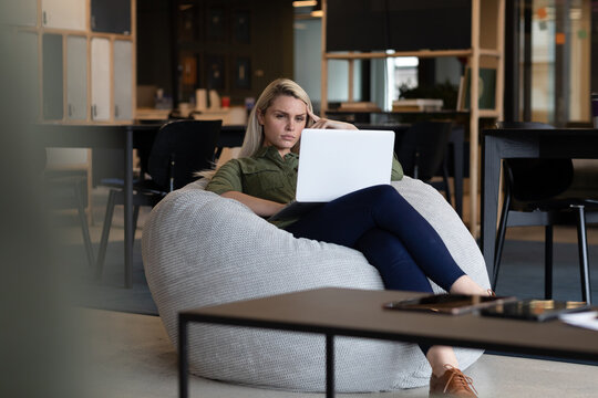 Caucasian businesswoman using laptop sitting in armchair in creative office