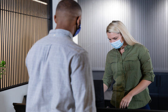 Caucasian female receptionist and male customer wearing face masks in office