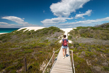 Woman walking along wooden footpath leading to sand dunes at De Hoop nature Reserve, South Africa.