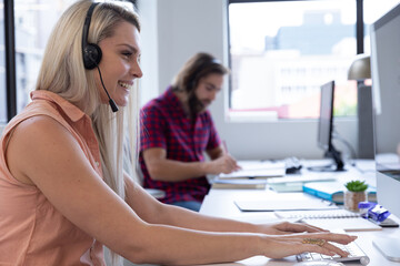 Caucasian woman wearing phone headset using computer in modern office