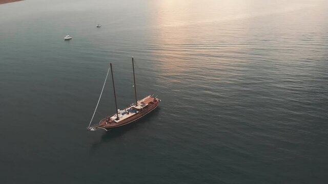 Aerial of two friends jumping from a wooden luxury sailboat during sunset